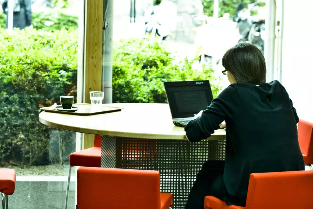 Person med laptop vid ett bord med utsikt över grönska. Foto